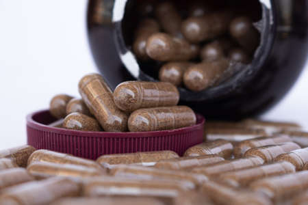 Amber plastic bottle with brown lid dropped open, with many pills of a drug or dietary supplement...