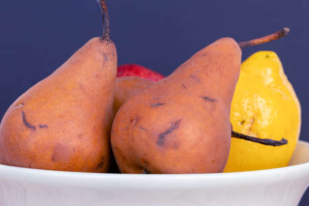 Pears of the Kaiser Alexander variety and other fruits in a white bowl on a wooden table and white...