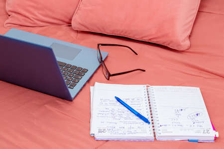 Open laptop, diary and glasses on a bed in a bedroom. I work from home, comfortable form of...
