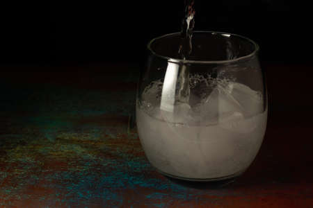 Glass of ice water being filled with sparkling water on a dark background and rustic surface.の写真素材