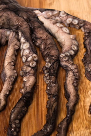 Detail of the tentacles of a small raw octopus stretched out on a wooden board.の写真素材