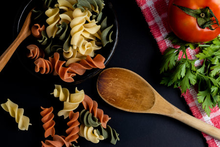 Ebano bowl with tricolor fusilli noodles and cherry and round tomato, chili peppers, garlic and parsley. Food raw material concept. Chopped angle. Close-up.の写真素材