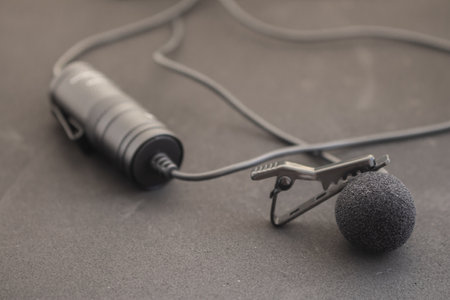 Lavalier or lapel microphone on a colored surface, very close-up. Details of the grip clip or fastener, mic power bank, miniplug, and wind sponge are visible. Concept useful object, sound production,の写真素材