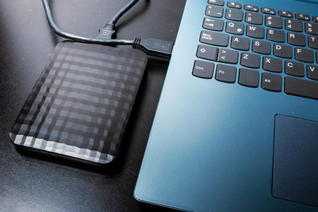 External hard drive with usb cable connected to a laptop or notebook computer on a black surface. concept technologyの写真素材