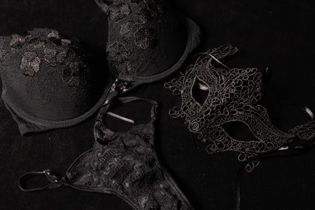 Venetian mask for a woman accompanying black female underwear on a black surface, concept of romanticism, mystery.の写真素材