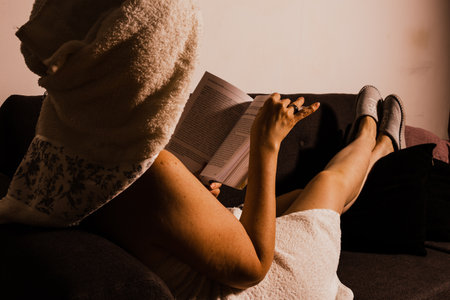 Unrecognizable woman lying on an armchair after bathing, resting and reading a book.の写真素材