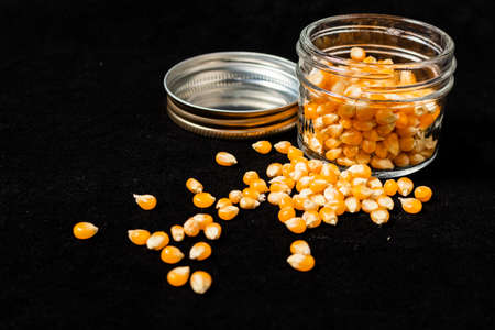 Orange corn seeds in a glass jar on a black surface. 45 deg. view