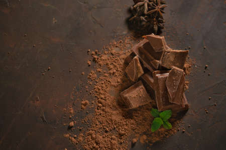 Different pieces of dark chocolate and cocoa powder on a dark surface. Mint leaves and star anise seeds complete the picture.の写真素材