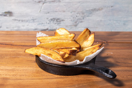 Rustic fried potatoes in a black iron pan on wooden table.の写真素材