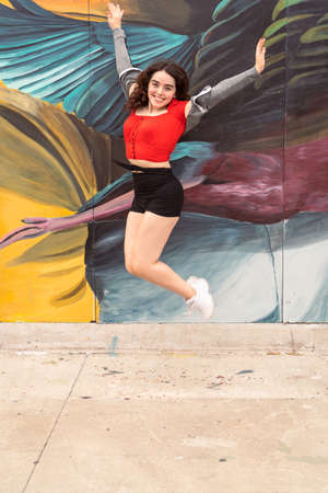 Beautiful happy smiling latinanamerican teenager jumping from happiness to celebrate, wearing red shirt and shorts.の写真素材