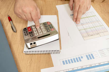 Sitting white man doing accounts with a calculator and reviewing cash and money flows, projections...