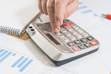 Sitting white man doing accounts with a calculator and reviewing cash and money flows, projections...
