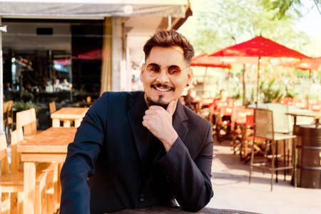 Young Latino man leaning confidently on a high table wearing sunglasses.の写真素材