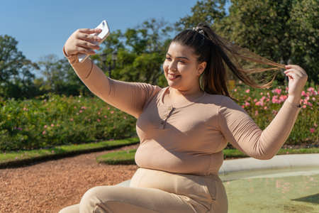 Beautiful young curvy girl taking a selfie while smiling happily.