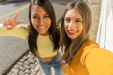 Two beautiful young women laughing while taking a selfie with their cell phone. Technology, communications, friendship concept.の写真素材