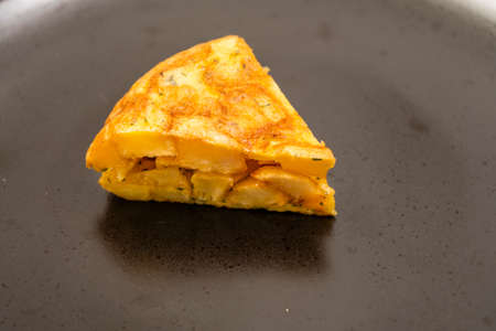 Normal close-up view of a serving of homemade potato or potato omelette on a black plate on a light marble table. Traditional tapas concept.の写真素材