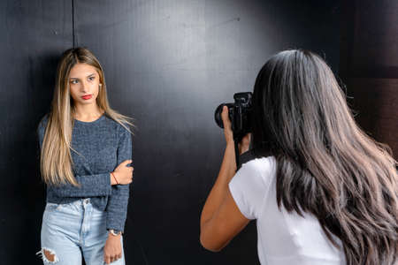 Horizontal portrait of a photo session of a model and a woman photographer in a photography studio, black background.の写真素材