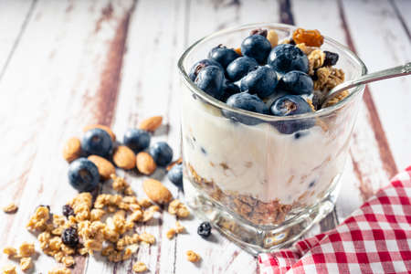 Normal view of a glass with a yogurt, blueberry and granola parfait on a rustic wooden table. Healthy and natural eating concept.の写真素材
