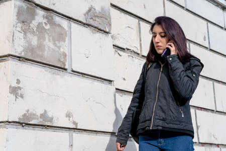 American shot of Young Latina woman walking and talking with a worried expression on cell phone in...