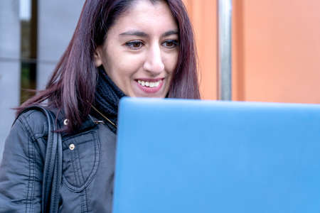 Portrait of a beautiful young Latina college woman smiling as she looks at her laptop screen outside...