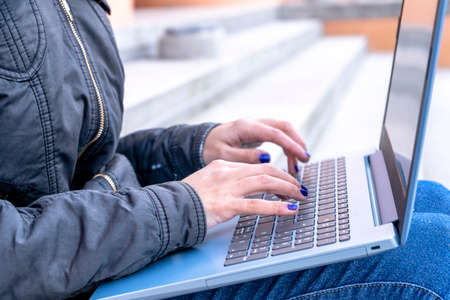 Hands of a woman working with a notebook or laptop on the stairs of a construction. Concept of work,...