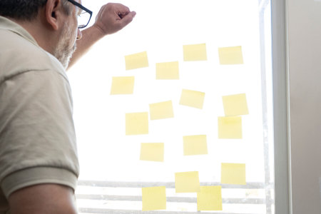 a man looking at note papers stuck to a window pane.の写真素材