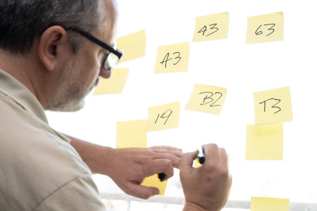 a man writing on some note papers taped to a window pane.