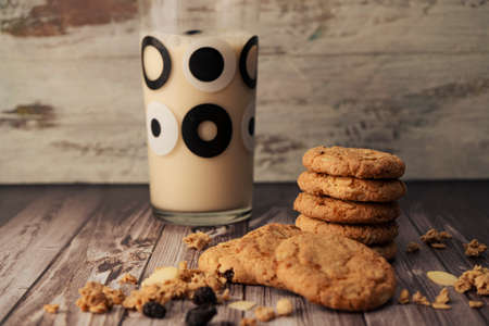 Stack of homemade oatmeal cookies with raisins and seeds, raisins and cereal dumped on the table and...
