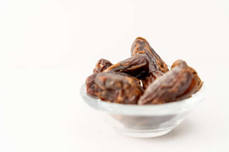 Fresh and organic dates in a small glass bowl on a white surface. Normal view, Concept healthy and...