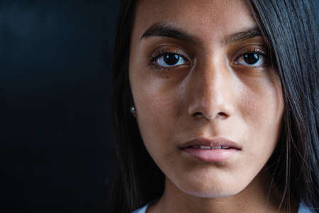 Close-up of a serious beautiful black haired Latina woman wearing a white T-shirt on a black...
