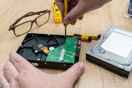 Hands of a man taking apart a broken hard disk. Technology concept.