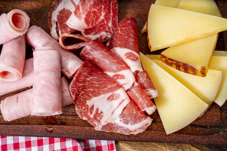 Cheese board and cold cuts on a wooden table. Zenithal or bird eye view.の写真素材