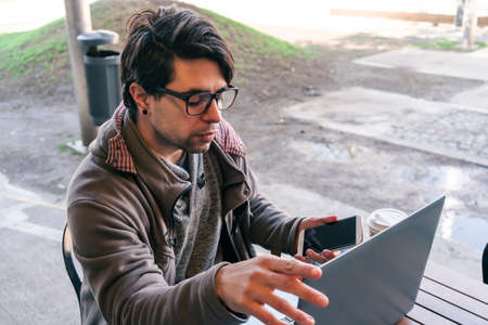 Mid-length shot of Man sitting at a bar while working on his laptop and checking his cell phone. teleworkingの写真素材