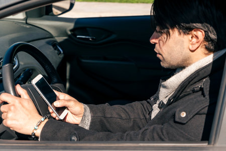 Attractive young businessman driving a car while answering a message on his cell phone. Danger and Road safety concept.の写真素材