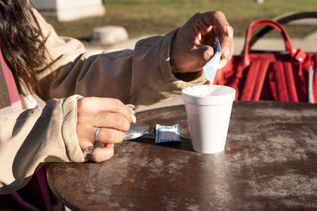 Woman adding sugar to coffee on the terrace of a cafe on a sunny day. Relaxation and free time...
