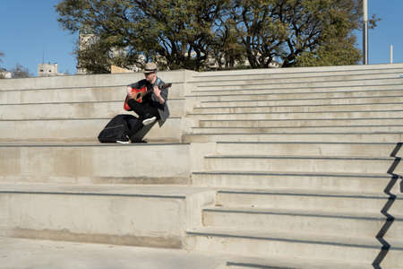 Shot of a man in a hat playing guitar sitting on some stairs in a public park. Copy space.の写真素材