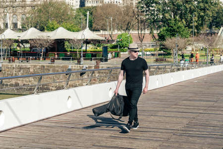 Distant shot of an albino man in a hat crossing a bridge with his guitar in hand. Concept or art, music.の写真素材