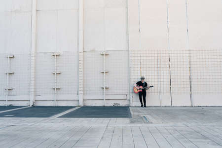 Albino man leaning against a wall while playing a song on his guitar. Concept of loneliness, remoteness, abandonment.の写真素材