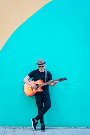 Close-up of albino man playing guitar leaning against a colored wall. Vertical orientation....