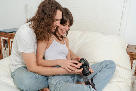 Couple reviewing photos in a dslr camera sitting in a bed in their house. joy concept.の写真素材