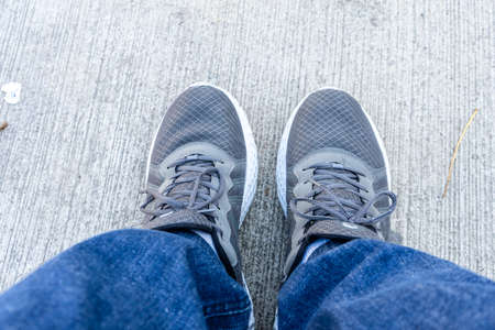 Feet wearing white chunky sole sneakers and blue jeans on the concrete floor viewed from above. New comfortable shoes for active lifestyle, fitness and sports. Top view.の写真素材