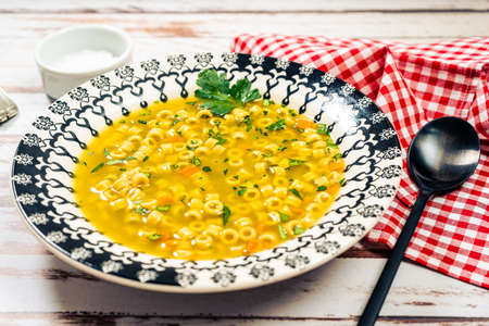 Minced view of an exquisite chicken and vegetable soup with small noodles and parsley, made at home. Served on a vintage plate on a rustic wooden table. Natural and healthy food conceptの写真素材