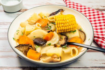 Minced view of an exquisite homemade chicken, vegetable and mushroom soup with noodles and corn. Served in a yellow bowl on a rustic wooden table. Natural and healthy food conceptの写真素材