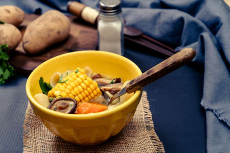 Minced view of an exquisite homemade chicken, vegetable and mushroom soup with noodles and corn. Served in a yellow bowl on a table with blue tablecloth. Natural and healthy food concept.の写真素材