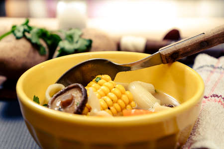 Minced view of an exquisite homemade chicken, vegetable and mushroom soup with noodles and corn. Served in a yellow bowl on a table with blue tablecloth. Natural and healthy food concept.の写真素材
