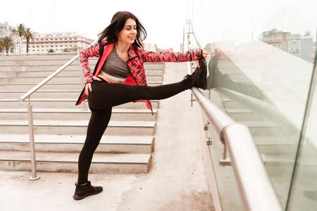 Young dark-haired athlete woman doing pre-stretching and warm-up to start running and doing...
