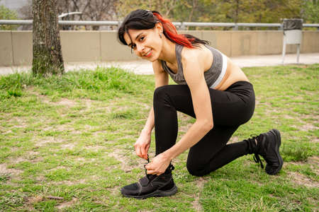 Portrait of an athletic woman tying her shoelaces and getting ready for jogging outdoors. Sport and...