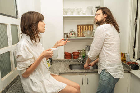 Young couple  talking in the kitchen  while the man washes the dishes.の写真素材