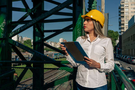 Beautiful young female engineer wearing a safety helmet and inspecting a railroad pedestrian bridge.