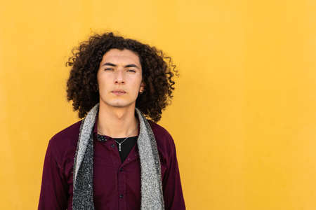 Short medium shot Portrait of a serious young Latino man in jean and burgundy shirt, with curly...